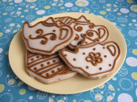 a pile of chai spice cookies shaped like tea pots on a pale yellow plate with a blue tablecloth