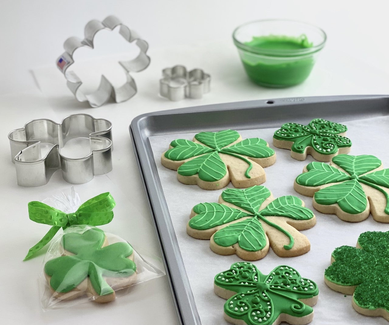 Shamrock cookies on a cookie sheet with assorted cookie cutters on a table