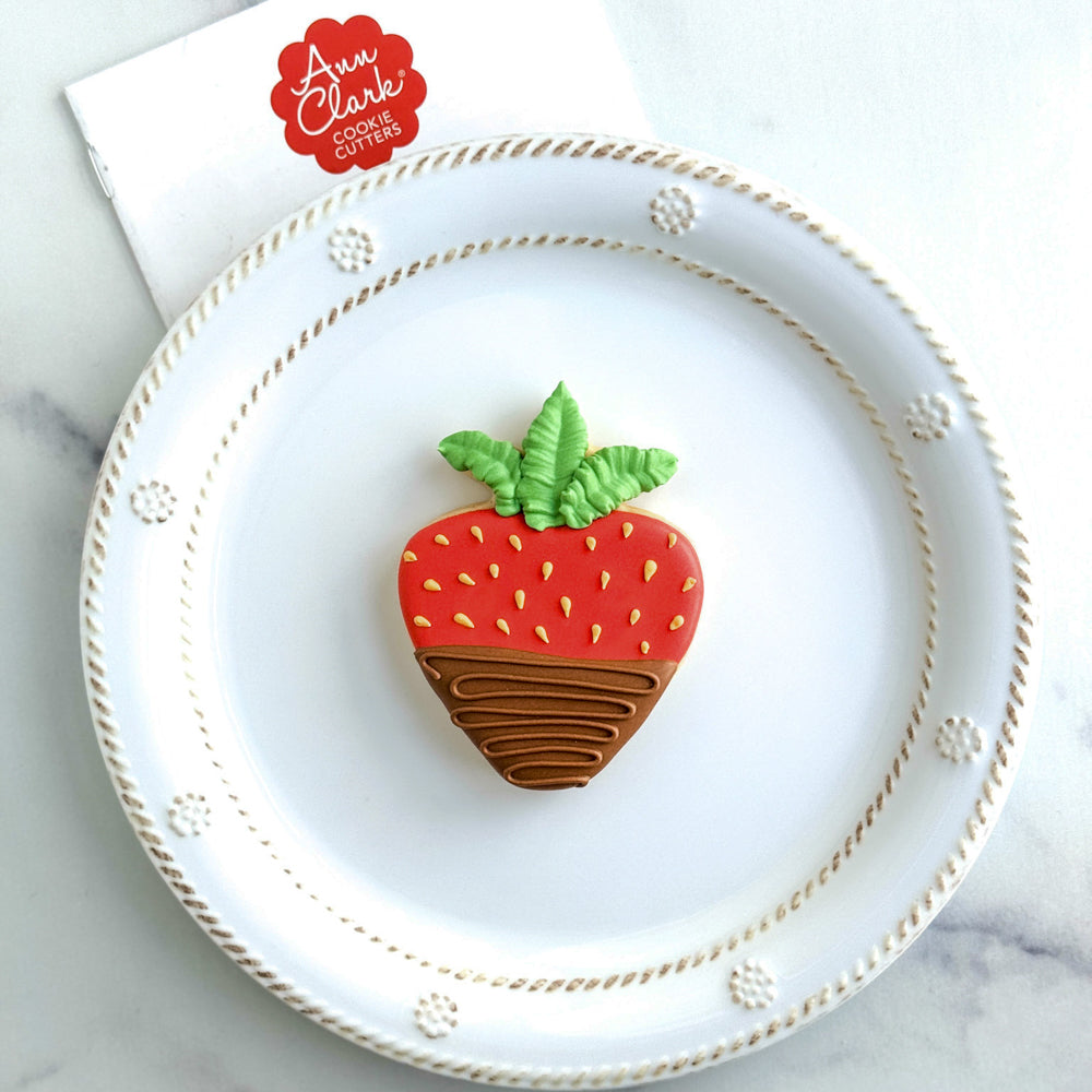 Image of a cookie decorated to look like a chocolate-dipped strawberry on a white plate.