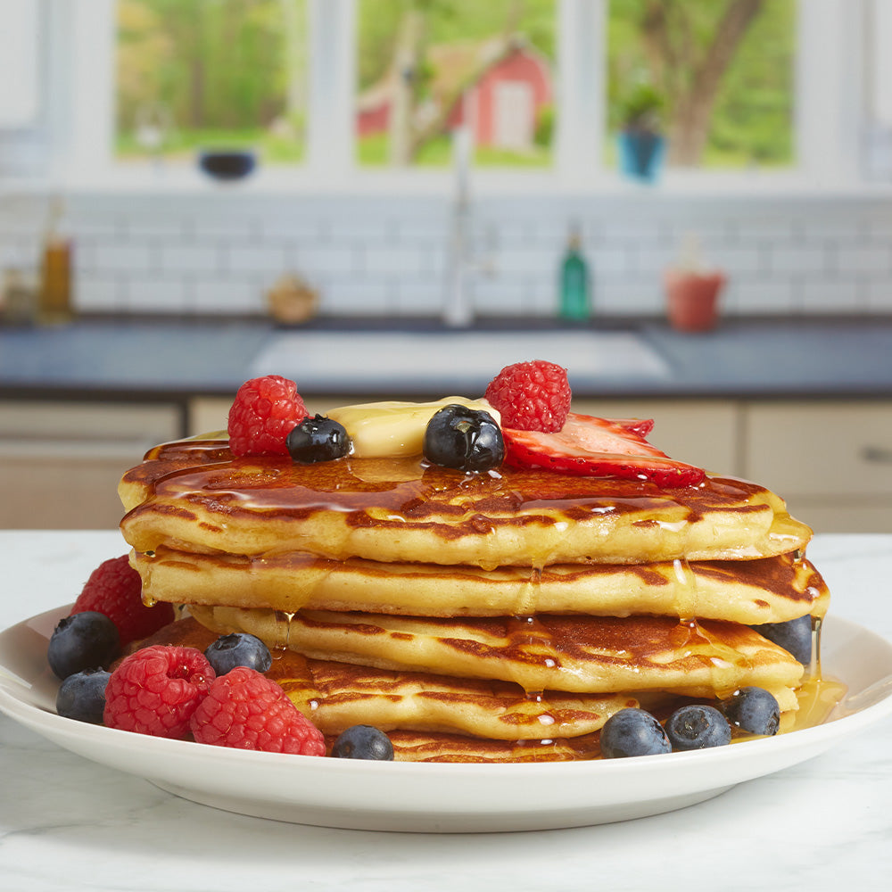 plate of pancakes with berries and maple syrup being poured over