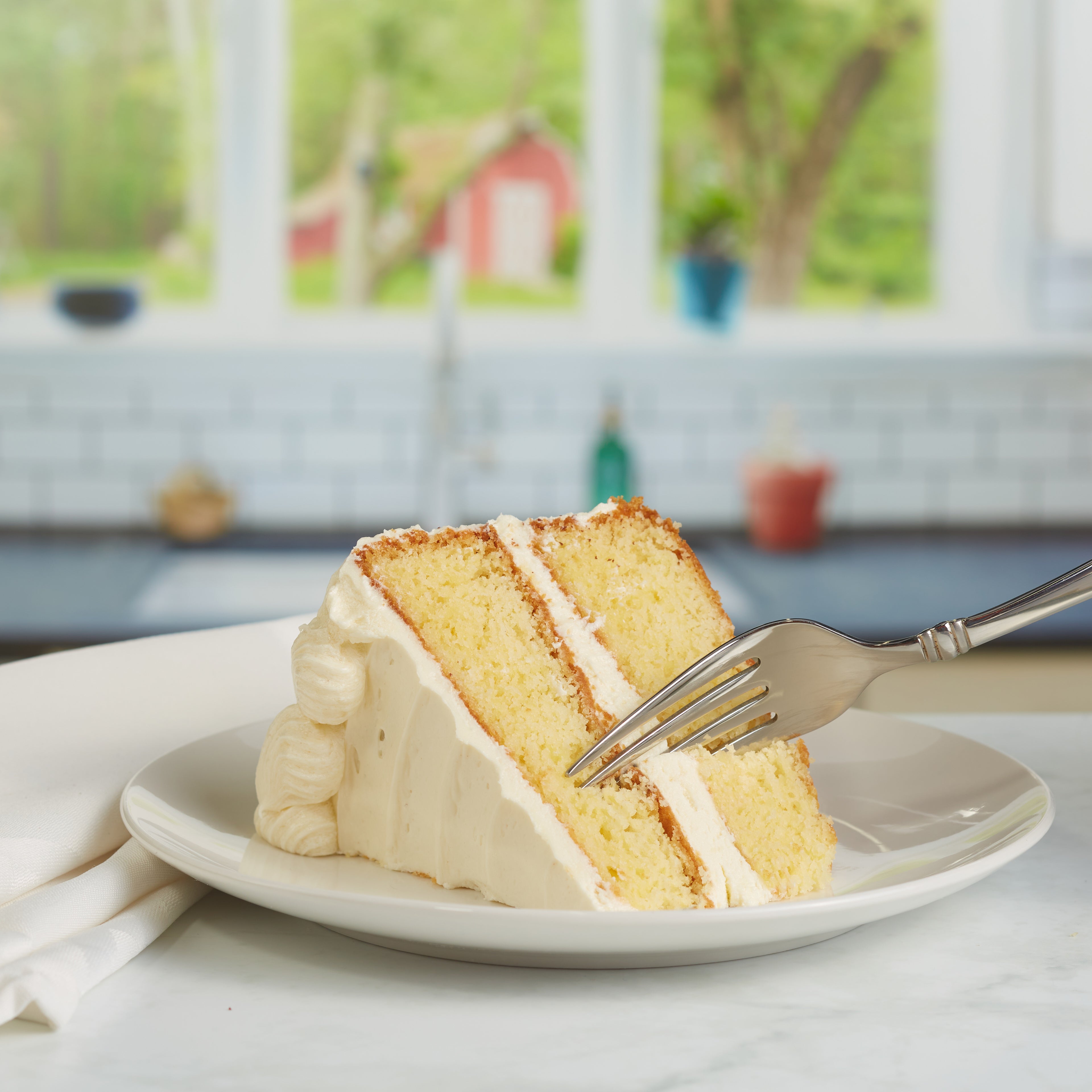 Image of a fork cutting into a slice of yellow cake with vanilla frosting