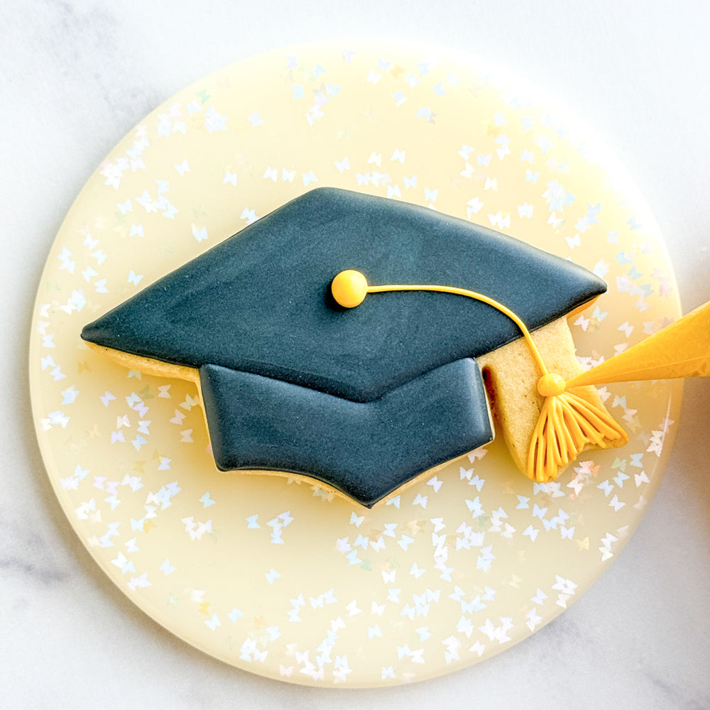Image of a graduation cap cookie decorated with black royal icing and a yellow tassel.