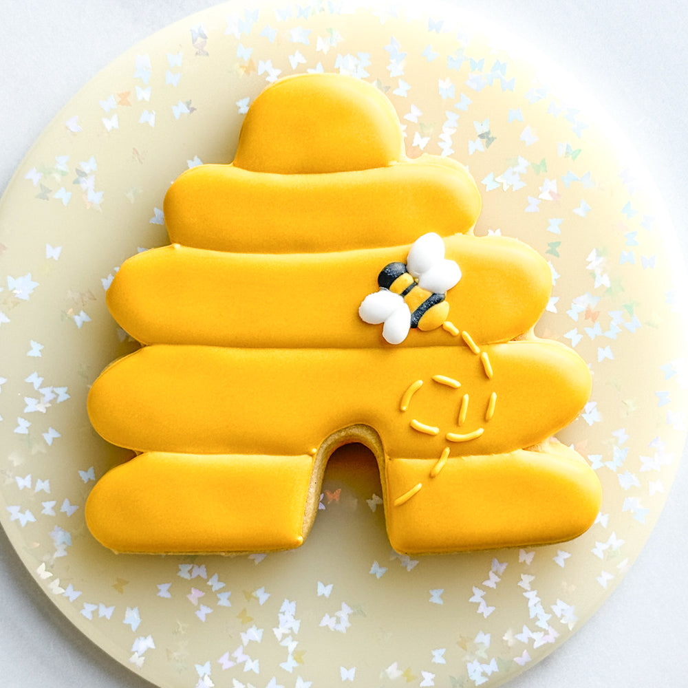 Image of a beehive cookie decorated with yellow royal icing and a bee royal icing transfer.