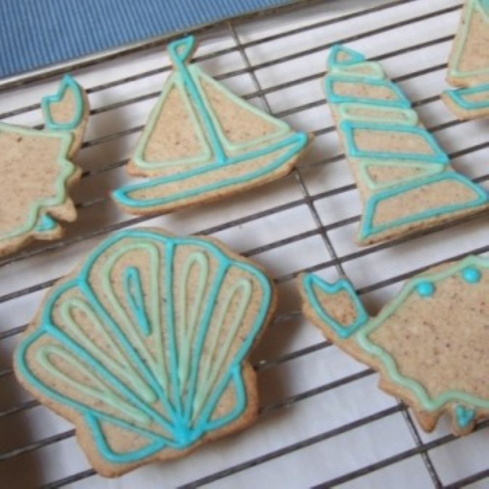 sailboat, seashell, and lighthouse shaped pecan sandies on a cooling rack decorated with teal and light green icing
