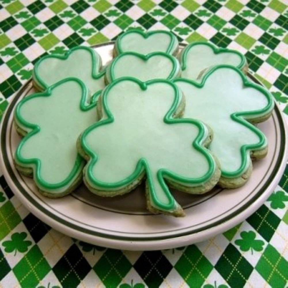 shamrock shaped cookies decorated in light and dark green icing on a plate with a green checkered tablecloth