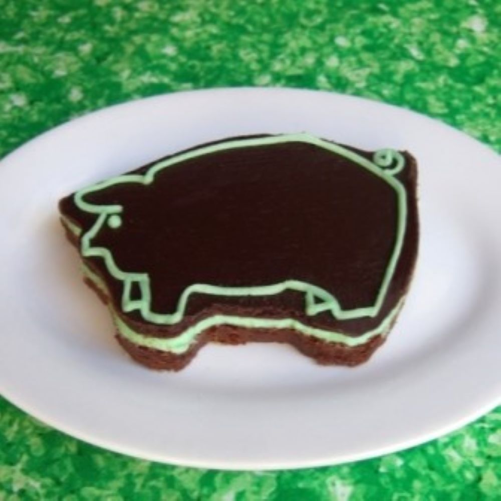 grasshopper brownie shaped like a pig with chocolate and green detail icing on a white plate with a green table
