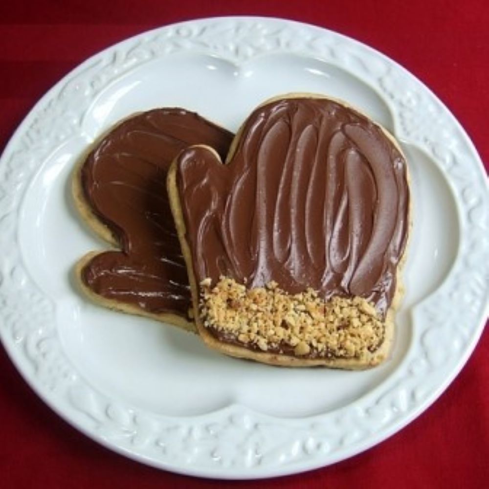 mitten shaped cookies covered with chocolate frosting and crushed nuts on a white plate