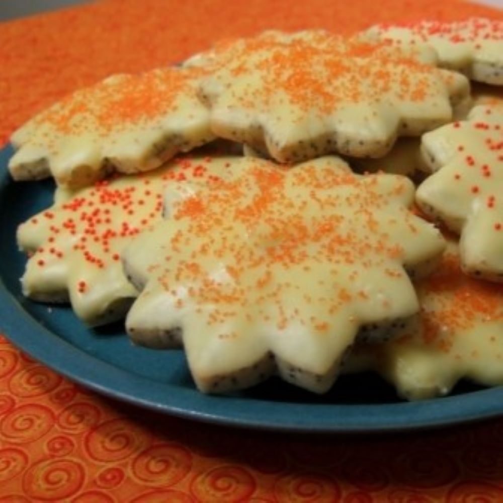 glazed orange poppyseed cookies shaped like a sunflower with orange sprinkles on a dark blue plate