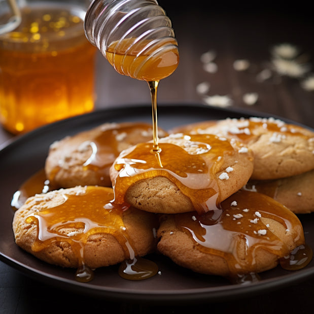 round cookies that are being drizzled with a honey glaze on a black plate with a jar of honey in the background