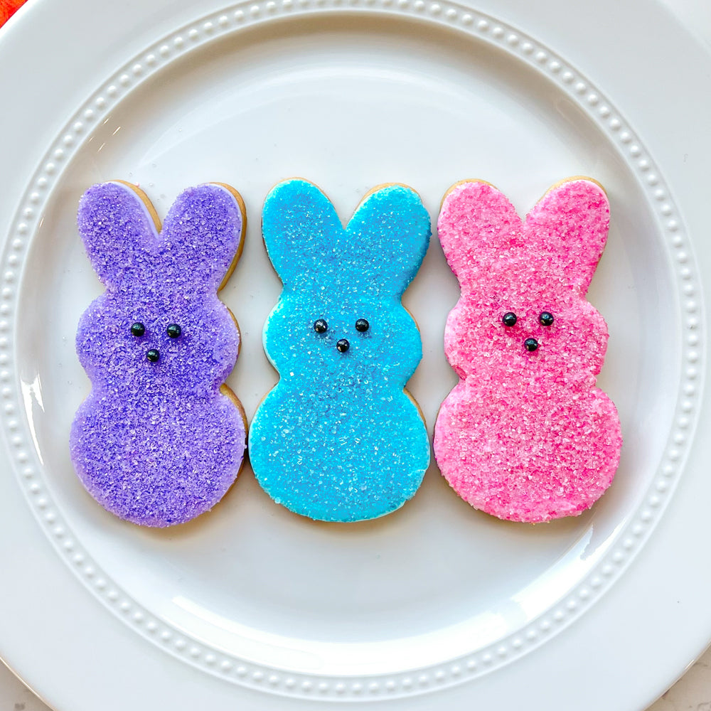 Three Easter bunny cookies decorated to look like colorful marshmallow bunnies on a plate. 