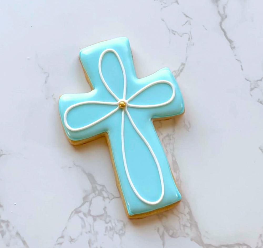 Sugar cookie decorated as a blue cross with a simple white embellishment on a marble countertop