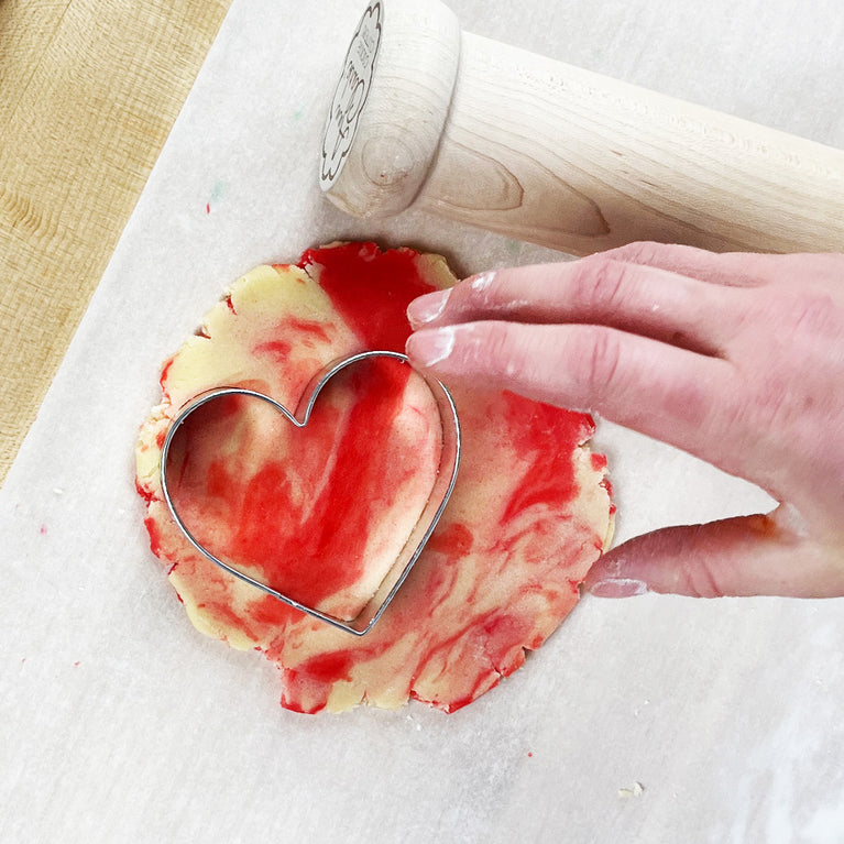 Hand cutting a heart shaped cookie with a heart cookie cutter