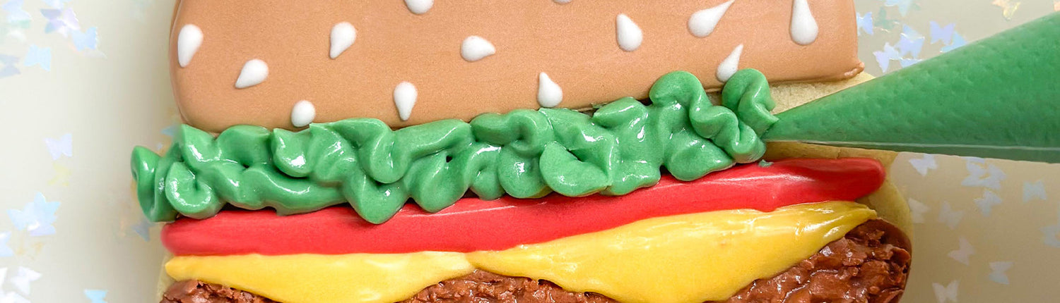 Piping bag decorating a cookie in the shape of a hamburger