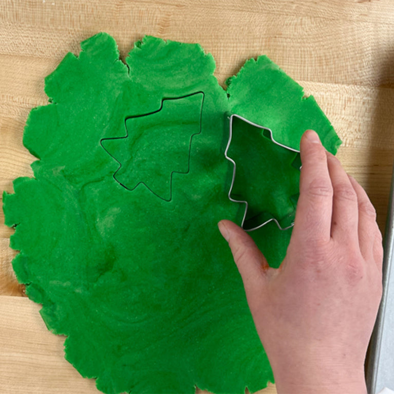 Green colored dough being cut out by a tree shaped cookie cutter