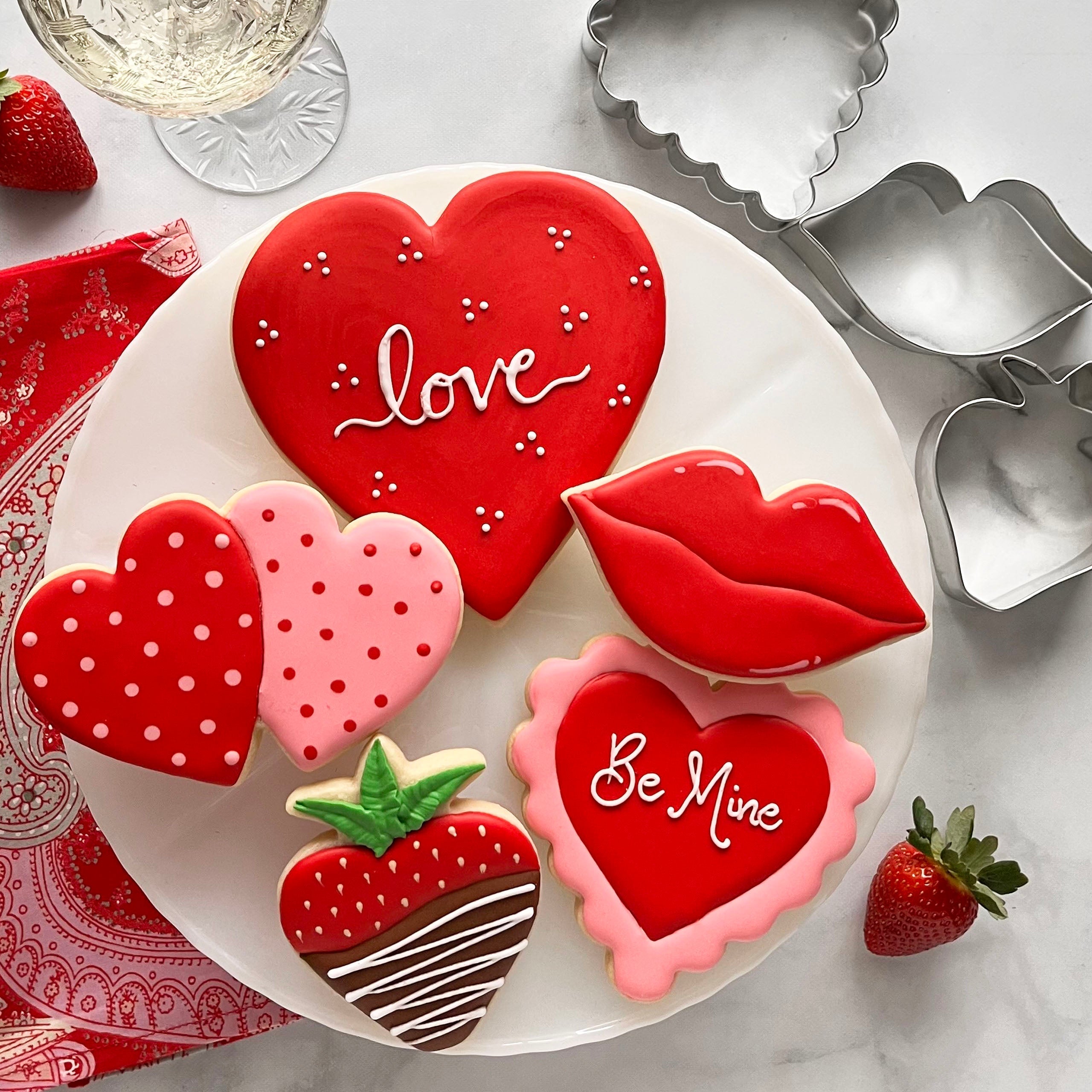 Heart and Valentine's Day related shaped cookies on a plate with assorted cookie cutters on a table