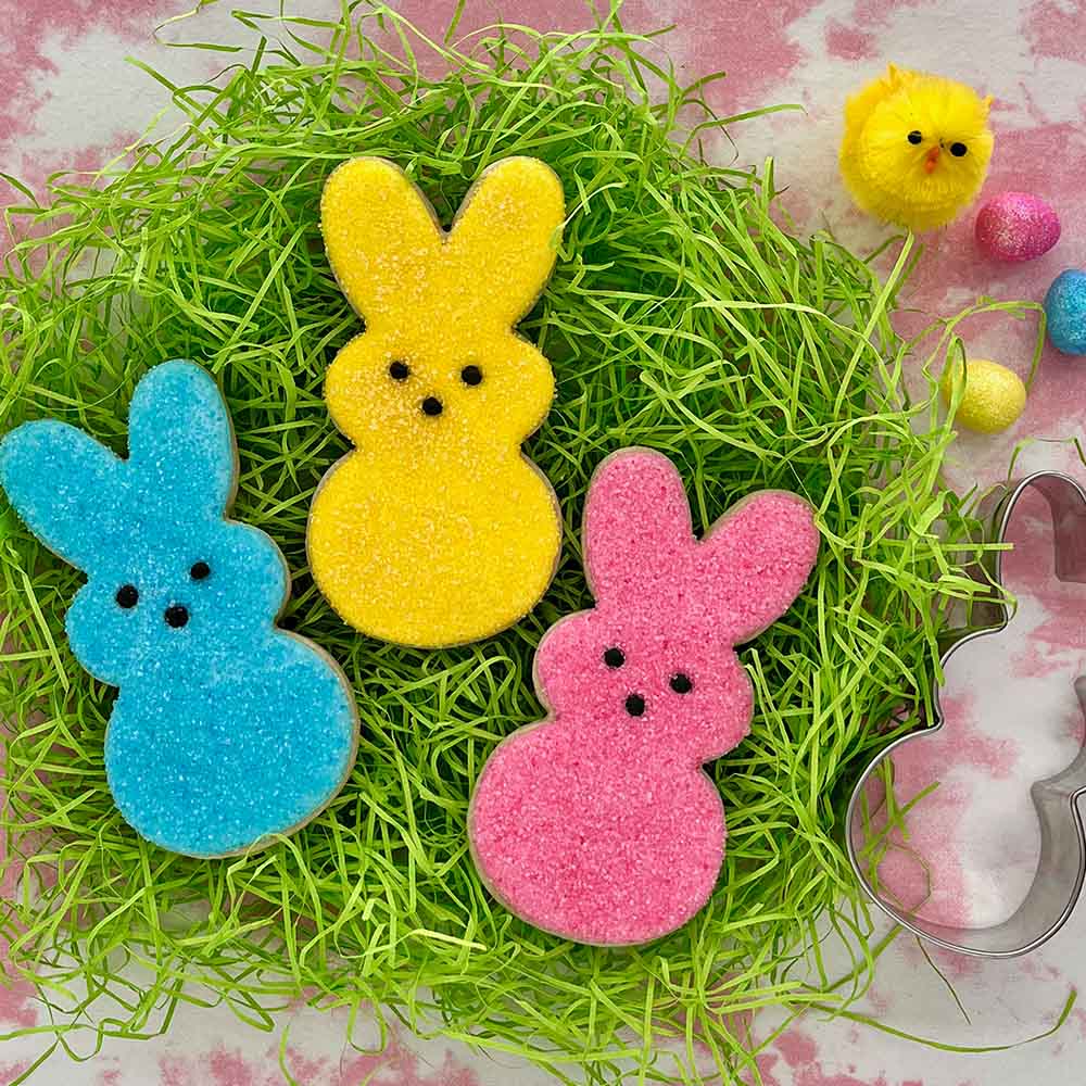 Three bunny sugar cookies decorated to look like marshmallow bunnies on a bed of fake grass