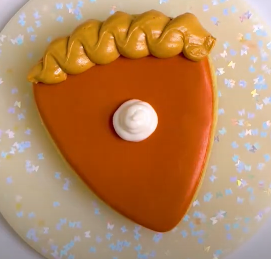 Image of a triangular sugar cookie decorated to look like a pumpkin pie slice.