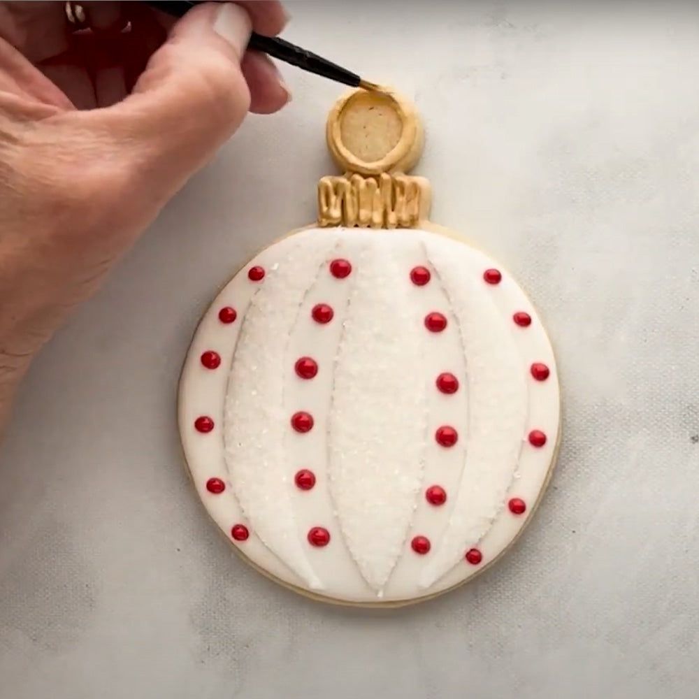 Hand decorating a white round ornament shaped cookie.