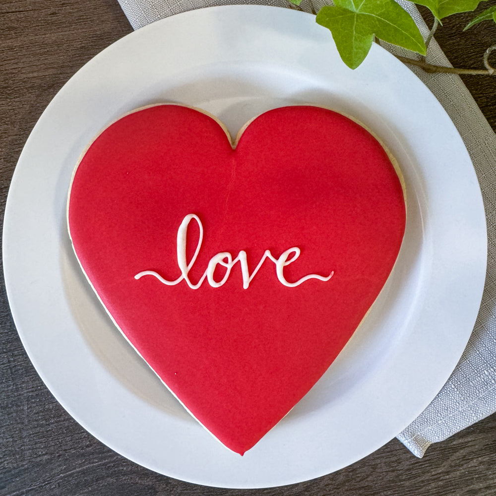 Image of a large red heart cookie with "love" written in script on it in white icing.