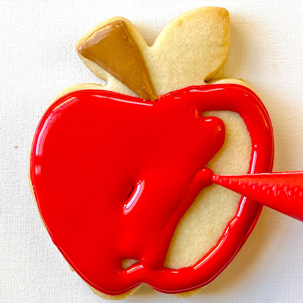 apple cookie being decorated with red royal icing