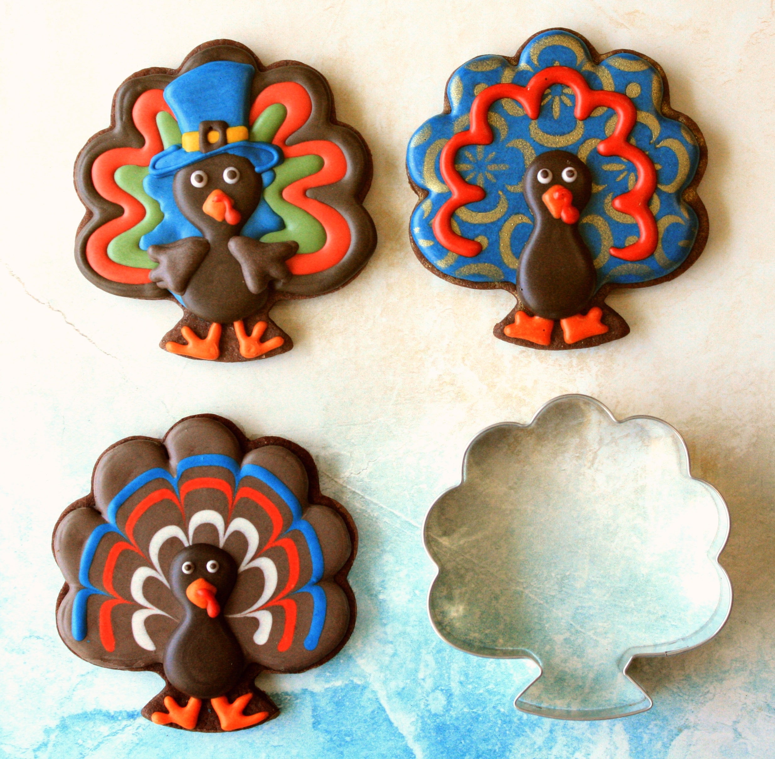 chocolate cookies shaped like turkeys with royal icing and a turkey cookie cutter on a white background