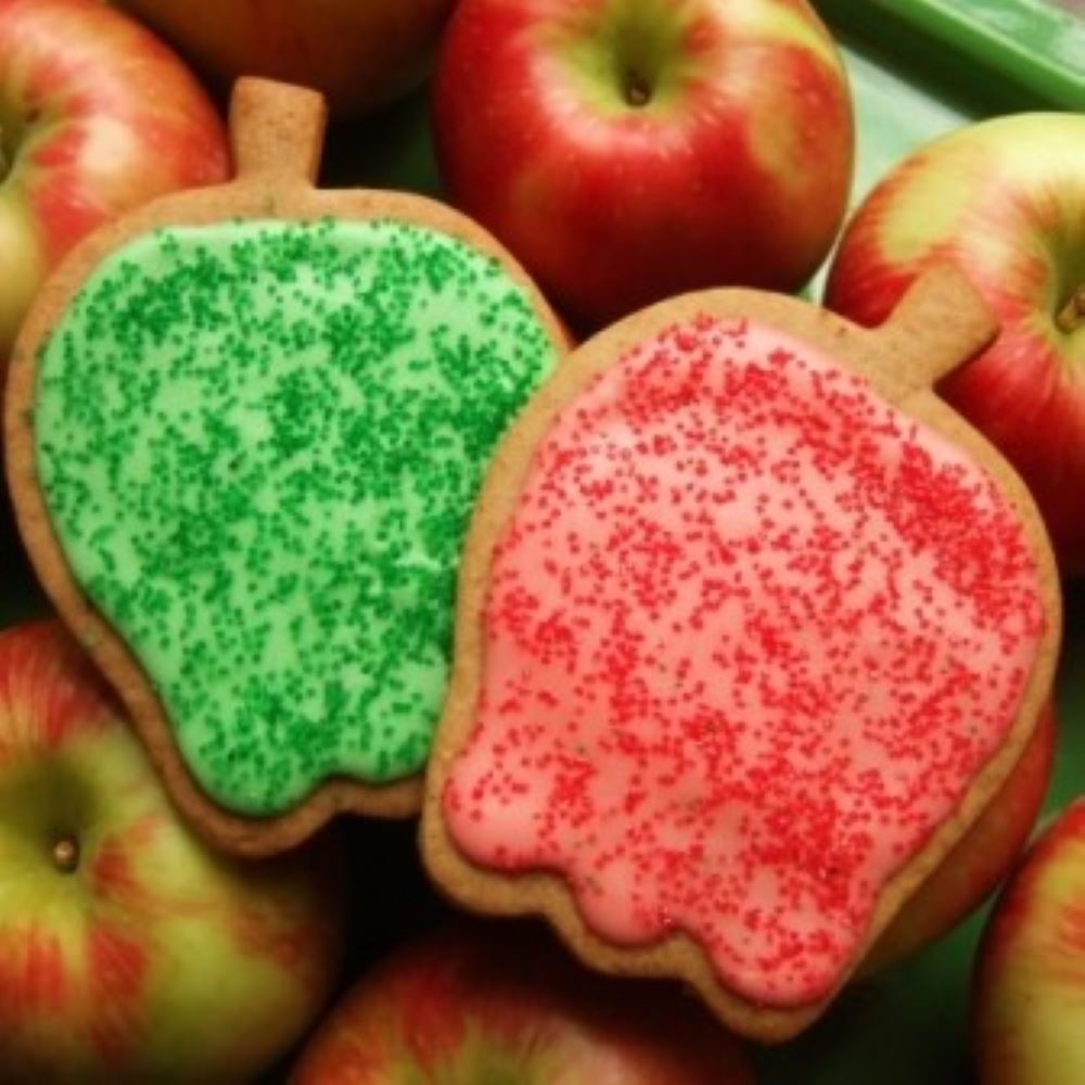 two apple shaped cookies with colorful glaze, sitting on top of a bunch of apples