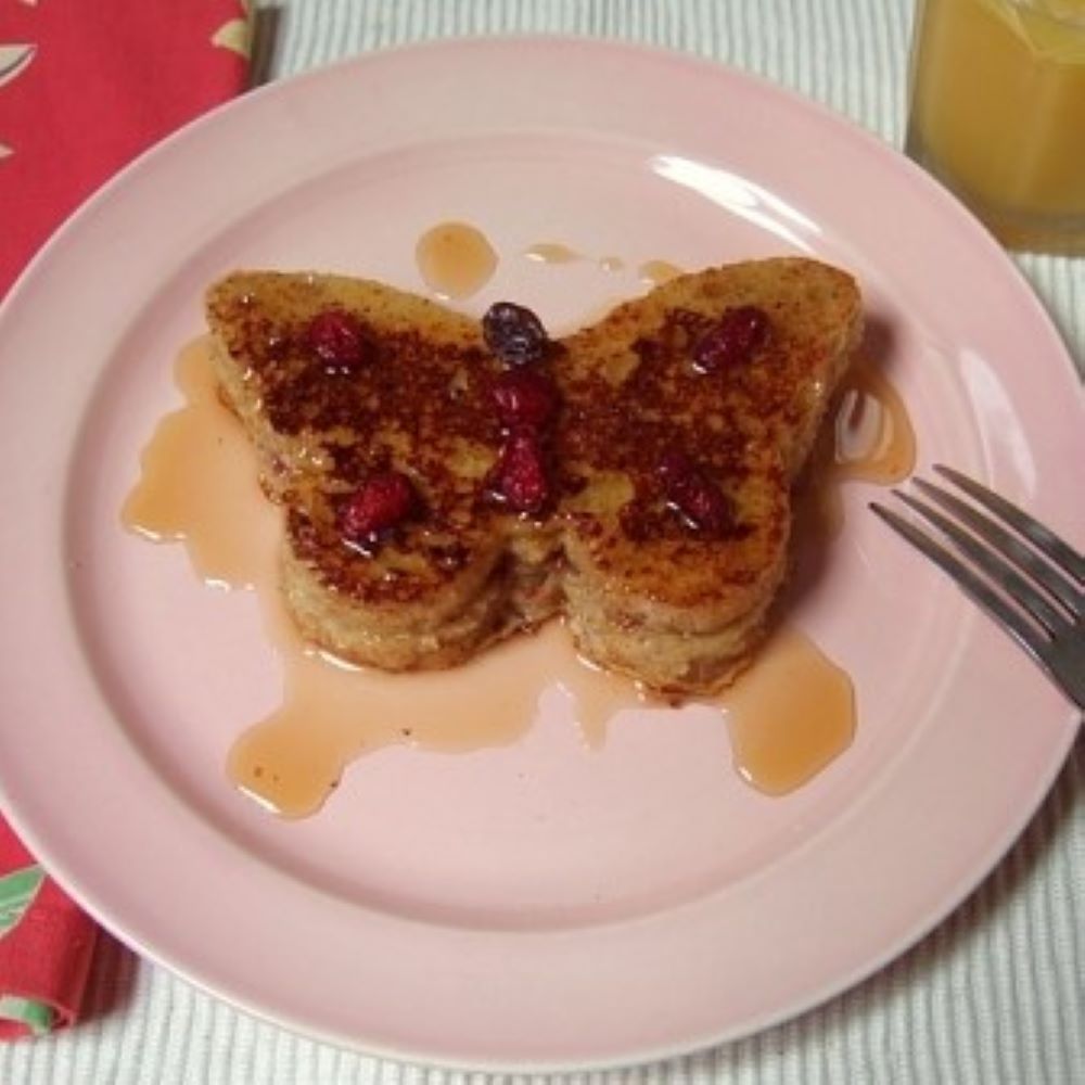 French toast sandwich in the shape of a butterfly covered in syrup on a blush pink plate