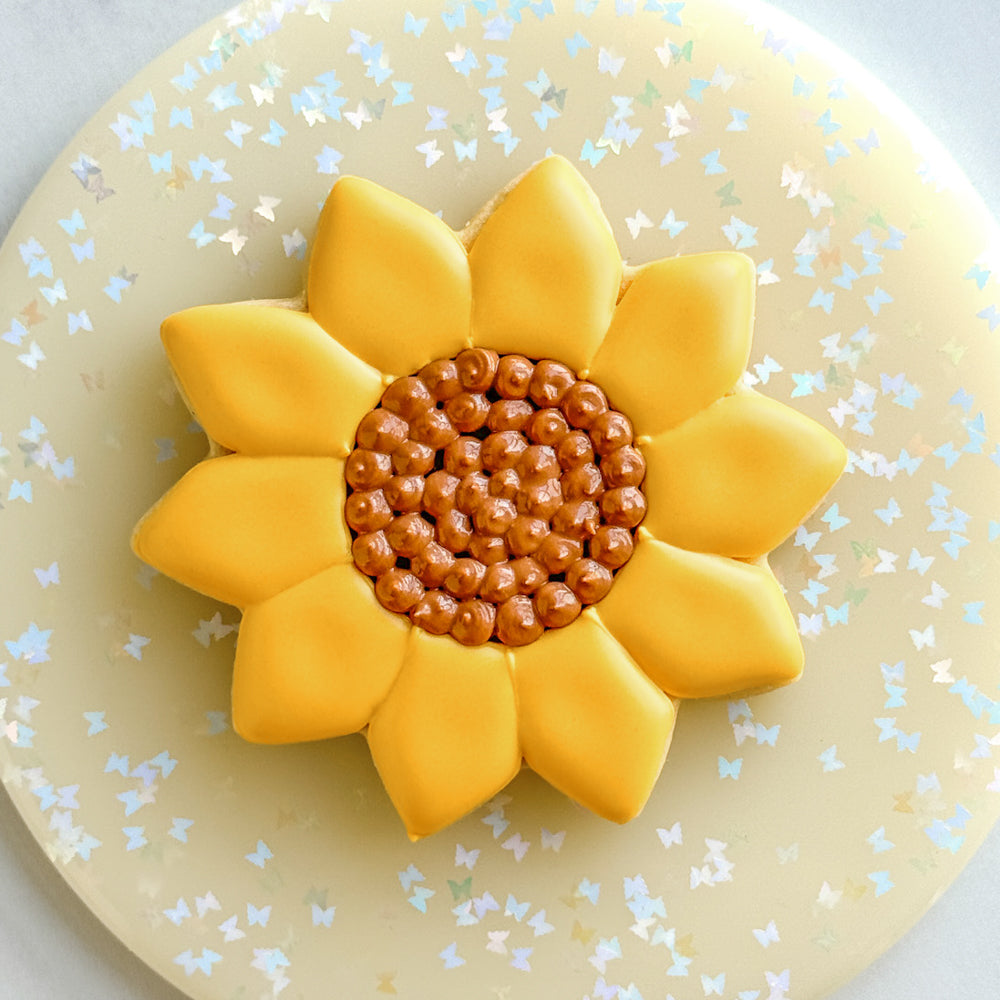 Image of a cookie decorated to look like a sunflower on a sparkly tray.