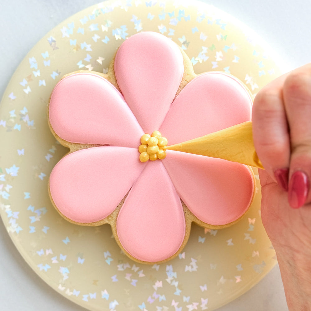 Hand decorating a pink flower with a yellow center
