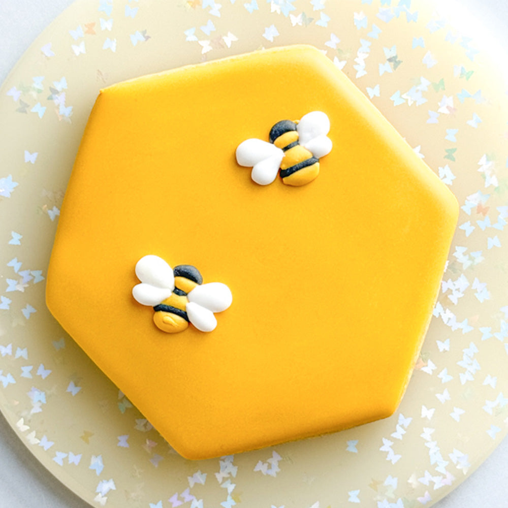 A yellow hexagon shaped cookie with bees on it