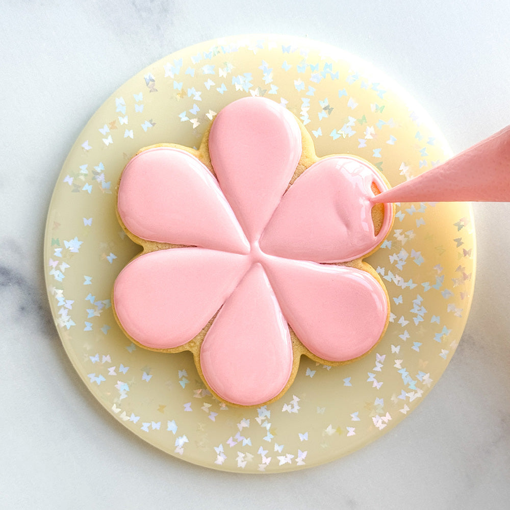 Flower shaped sugar cookie being decorated with pink icing