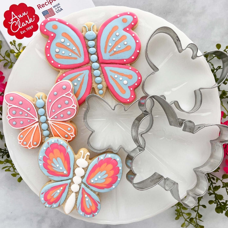 Brightly decorated butterfly cookies and butterfly cookie cutters on a white plate