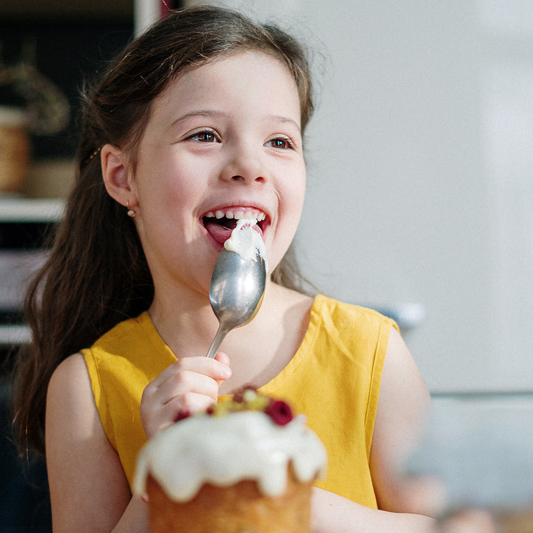 Smiling girl licking spoon covered in frosting