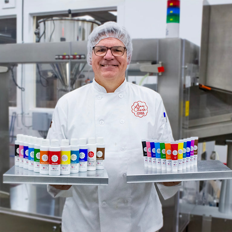 Man standing in front of industrial food prep machinery with two trays of food coloring gels