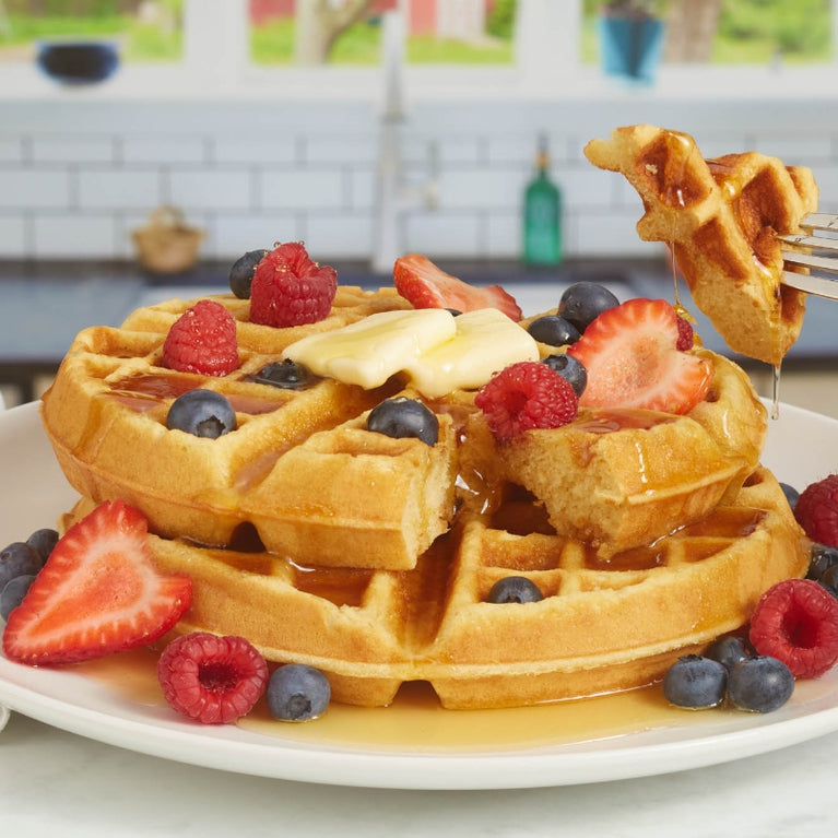 Fork lifting a slice of waffles topped with syrup and berries