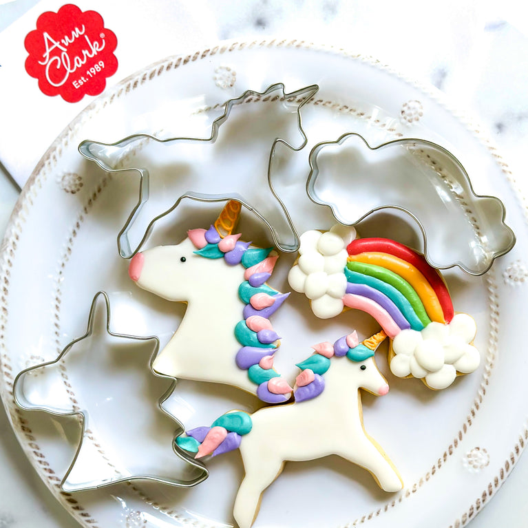 Decorated unicorn cookies on a plate with cookie cutters
