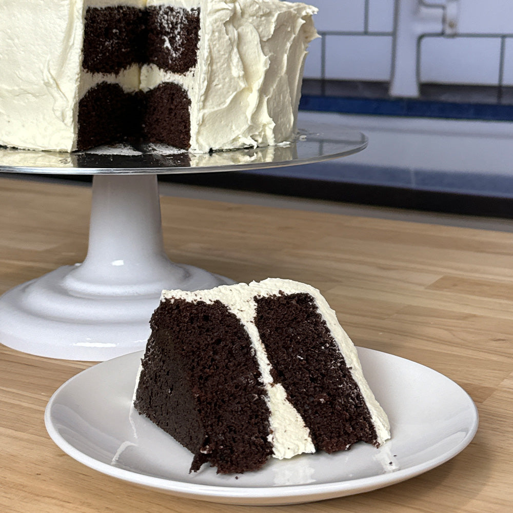 Slice of chocolate cake with vanilla frosting on a white plate