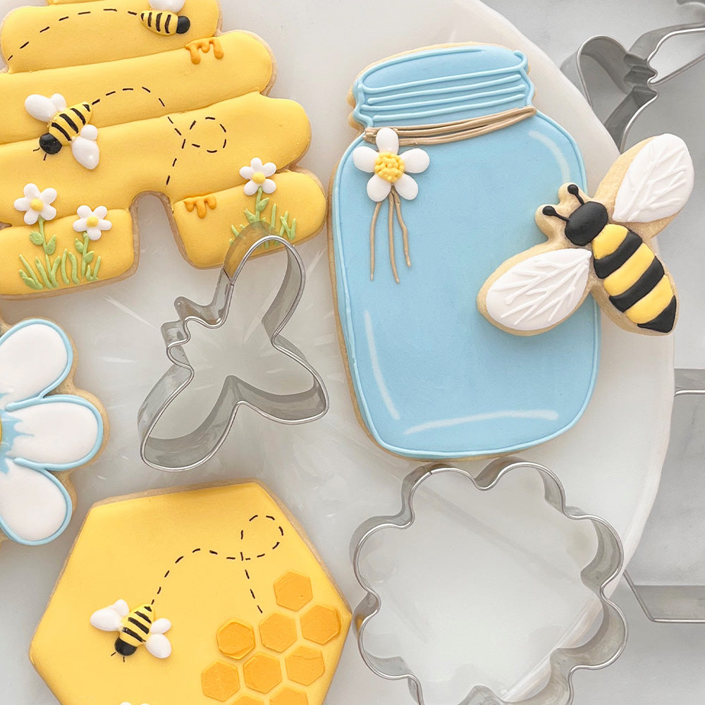 Mason jar, beehive, and bee shaped cookies and cookie cutters on a white plate